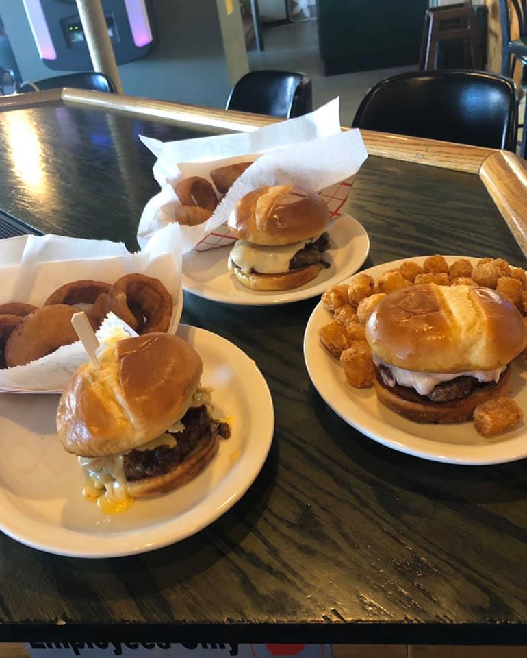Three burgers, two with a side of onion rings and one with tater tots