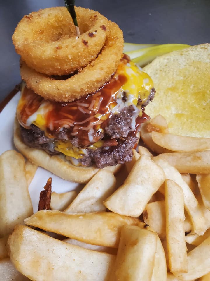 A burger with onion rings stacked on top with fries