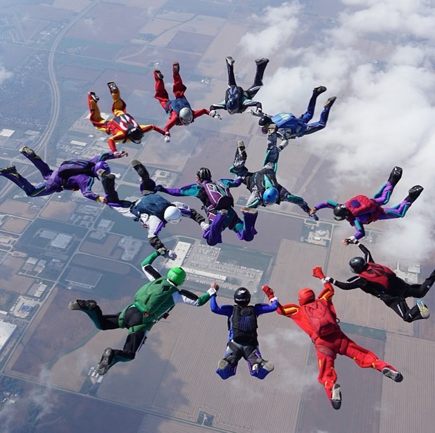 a group of skydivers holding hands in a circle in the air 