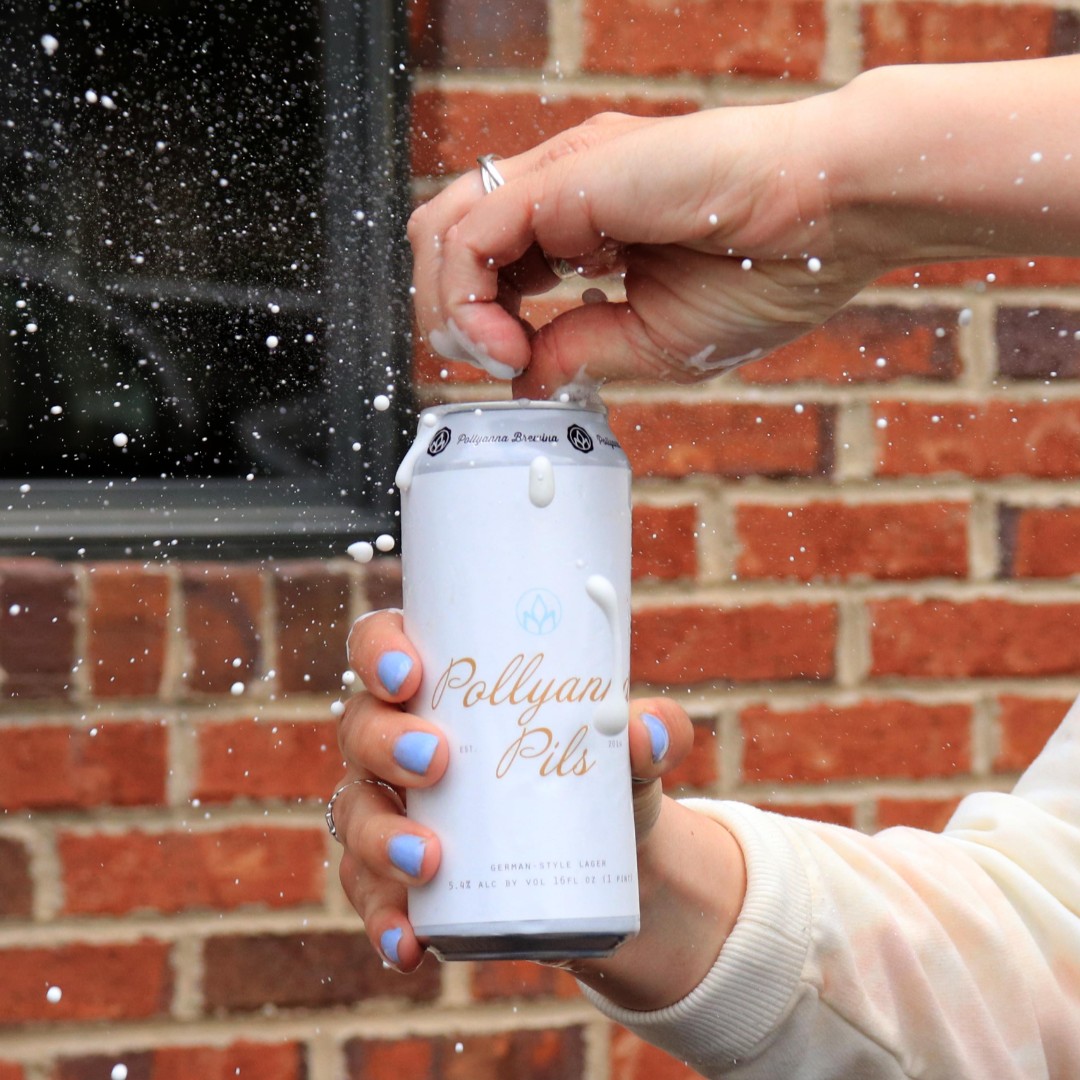 Someone opening a can of Pollyanna Pils, with some foam spitting out