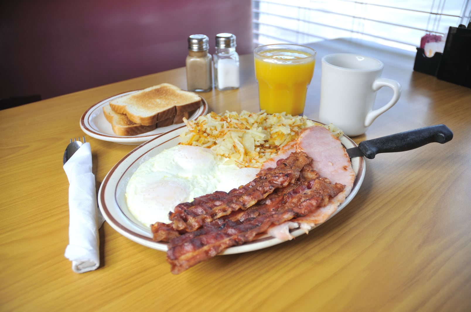 fried eggs, bacon, hame, hash browns, and toast with a cup of coffee and orange juice