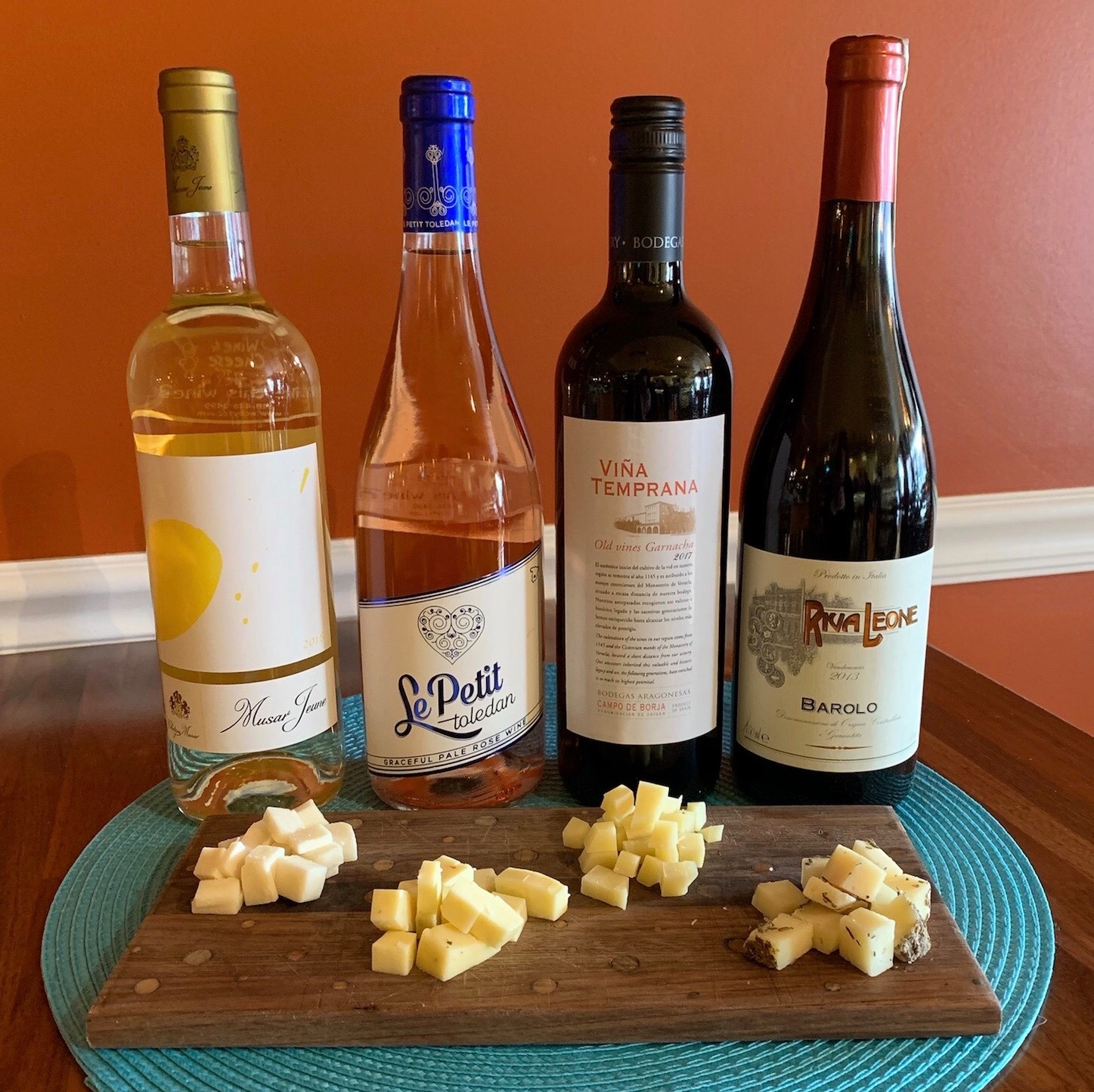 4 bottles of wine next to a board of cut up cheese