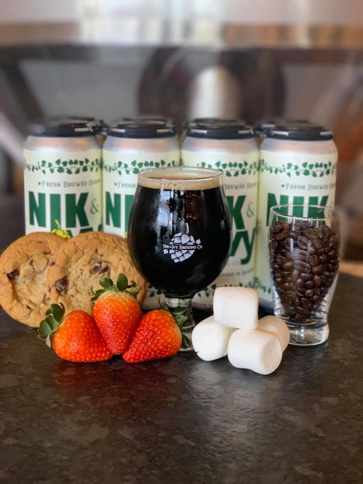 Nik & IVy's Chocolate Fondue Beer (surrounded by a glass of cocoa beans, marshmallows, strawberries, and  four cans)